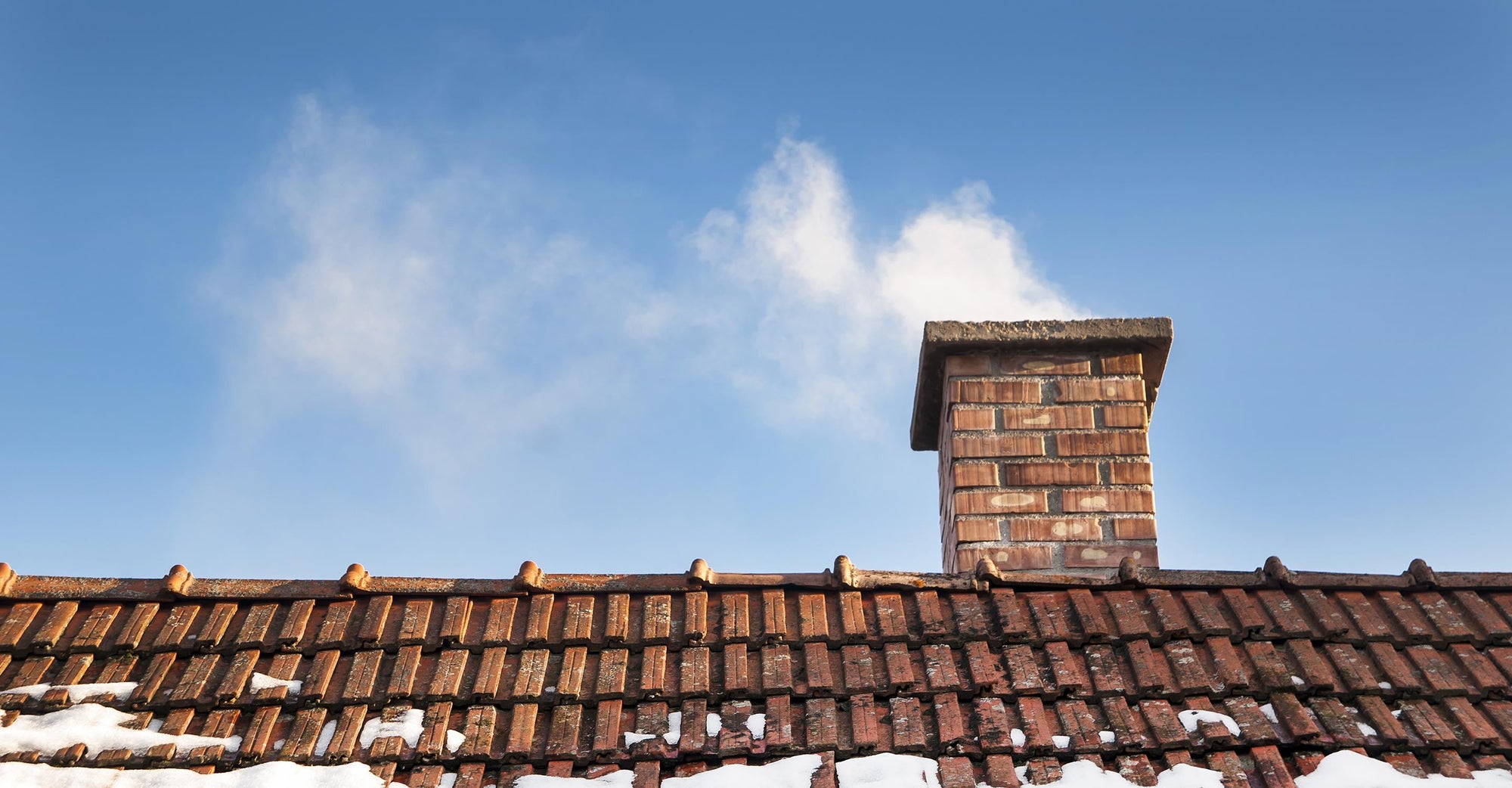 A close up of a smoking chimney atop an old home.