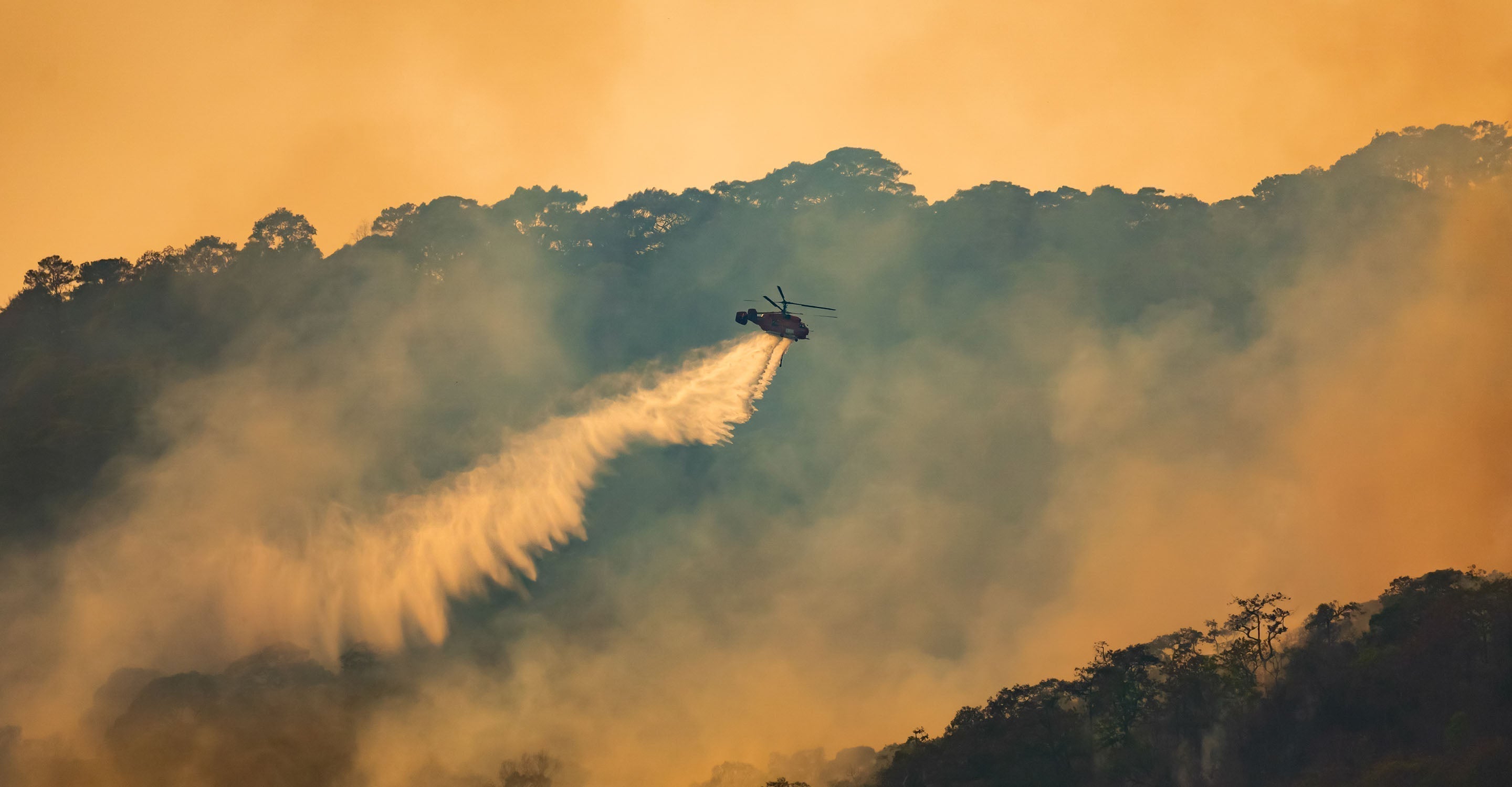 Helicopter drops fire suppressant over forest